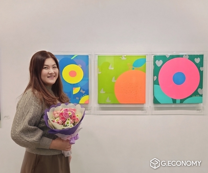 작가 리강(이강연)이 전시 축하 기념 꽃다발을 들고 활짝 웃으며 기념촬영. 뉴스아이이에스
