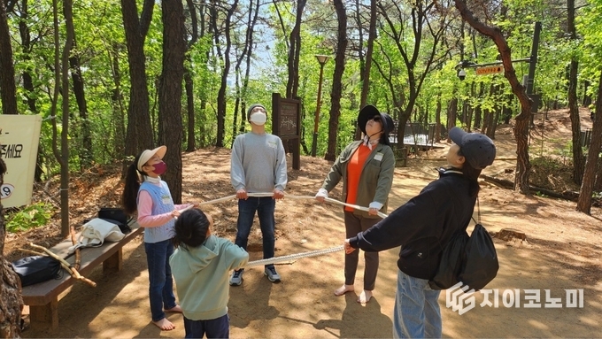 가족 단위 참가자들이 숲에서 밧줄을 이용한 활동을 체험하고 있다.