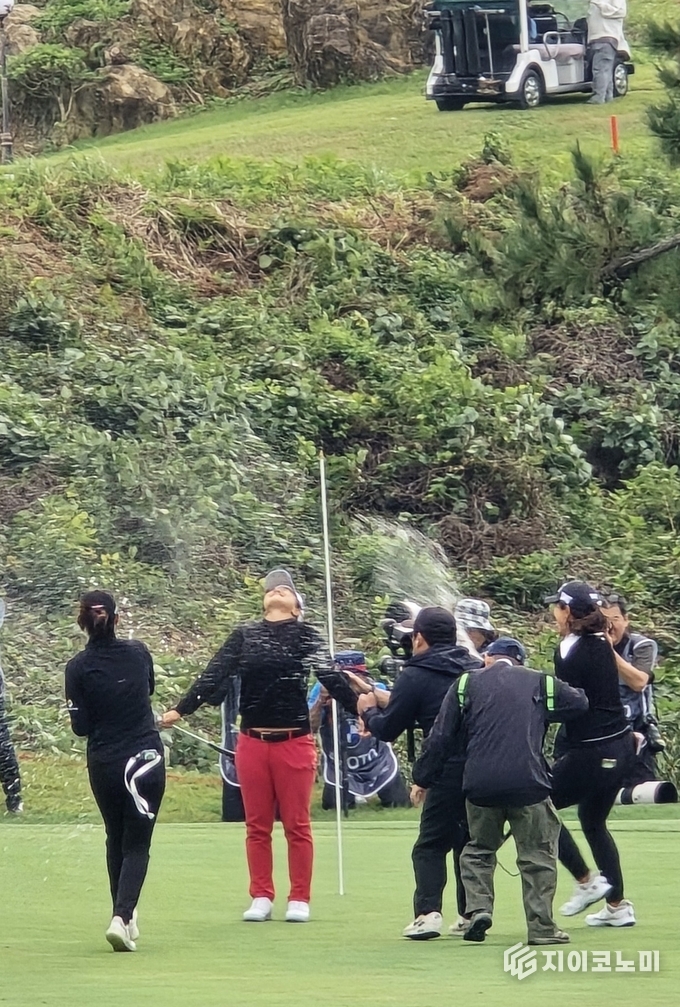 김세영이 우승 퍼트를 마친 직후 두 팔을 번쩍 들어 올리며 환호하고 있다. 갤러리의 환호가 파도처럼 번져나가는 가운데, 동료 선수들과 캐디의 축하 인사가 이어지며 5년 만의 우승 세리머니가 해남의 바람 위로 터져 올랐다. G이코노미DB